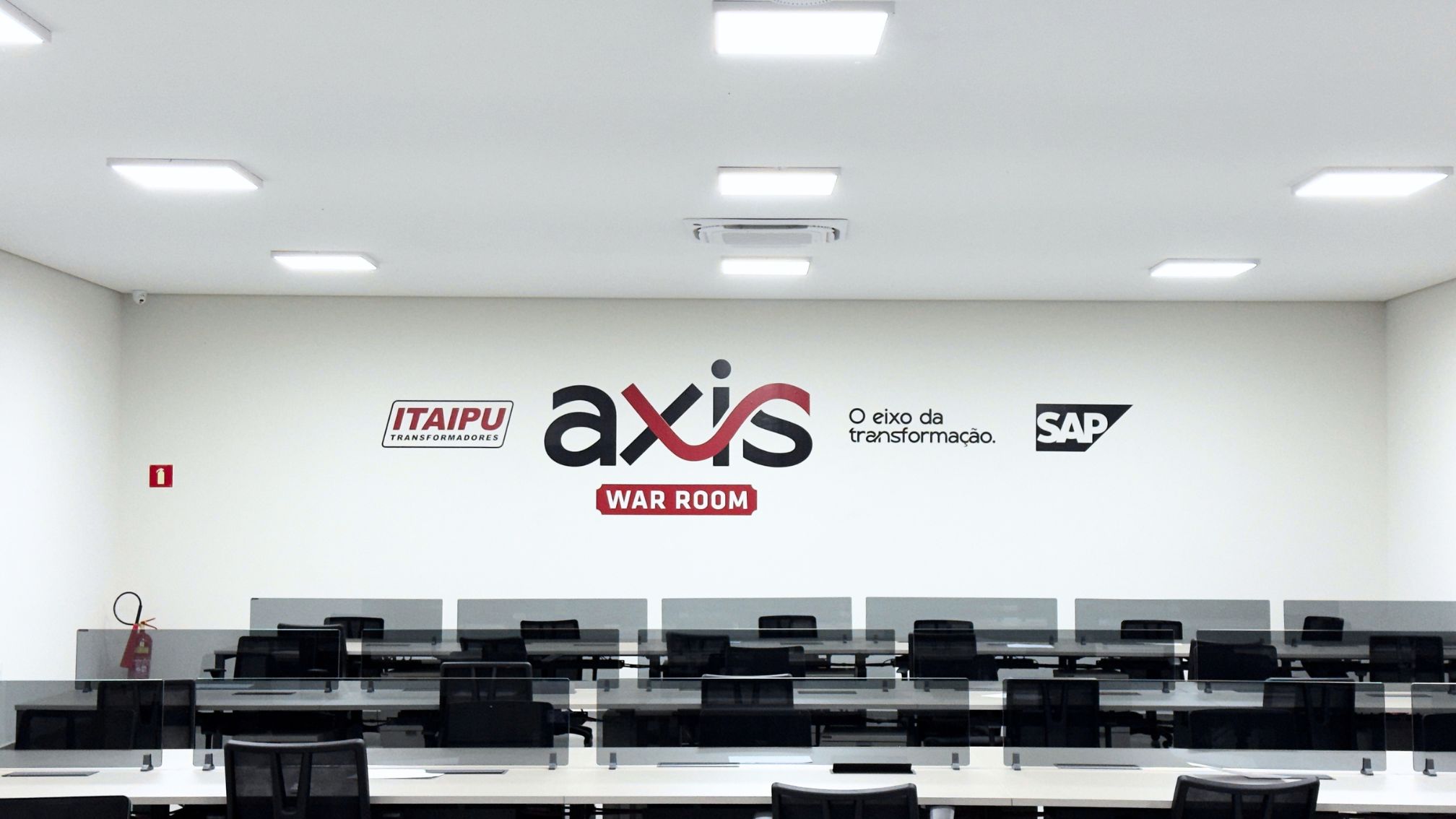 Sala do projeto AXIS com estações de trabalho e identidade visual na parede